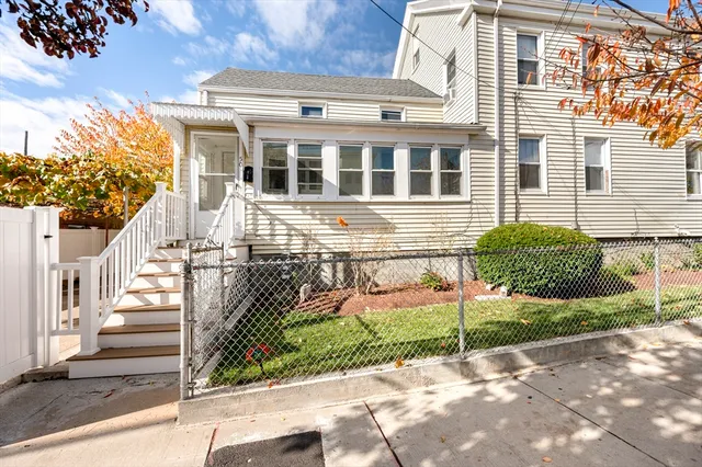 a view of a white house with a large tree and wooden fence