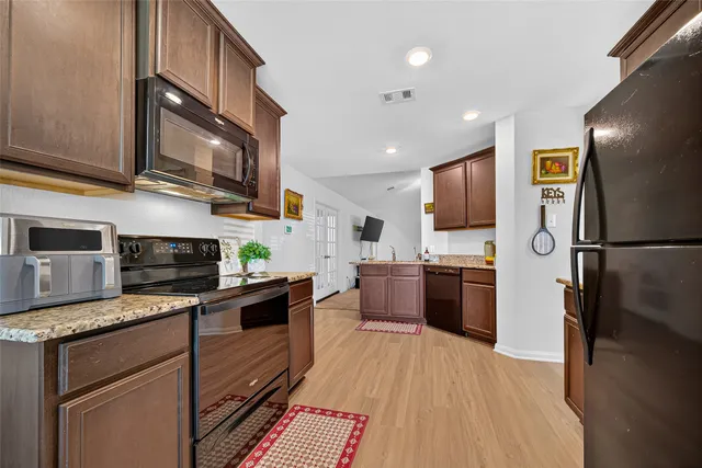 a kitchen with stainless steel appliances granite countertop a refrigerator a stove top oven a sink dishwasher and wooden cabinets with wooden floor