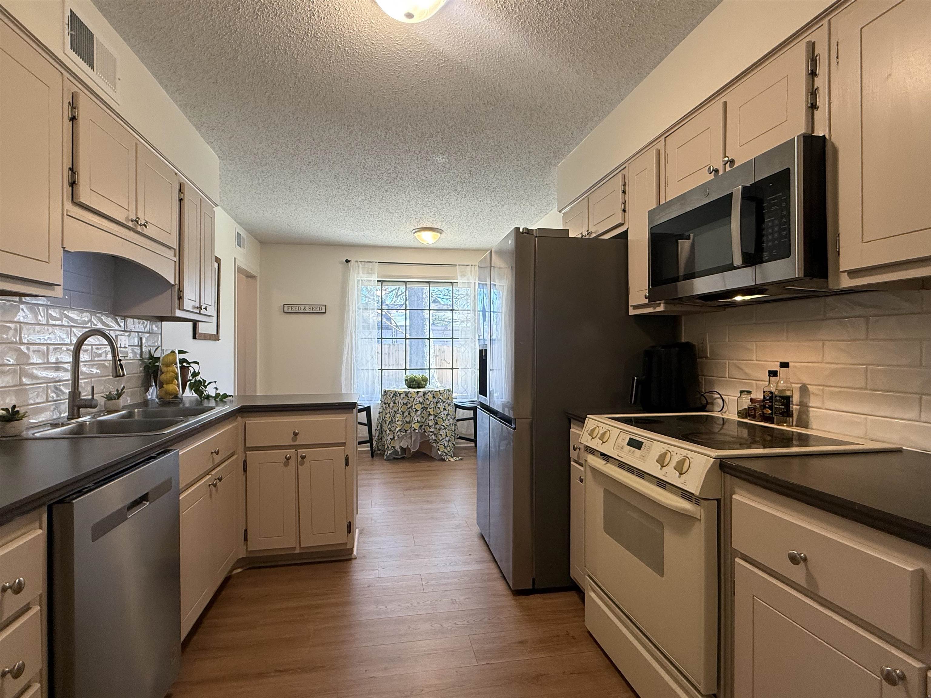 3204 Ruskin Road Memphis, TN 38134 - Photo 22 of 38 Kitchen featuring stainless steel appliances, tasteful backsplash, dark countertops, light wood finished floors, and a textured ceiling