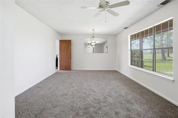 an empty room with chandelier fan and windows