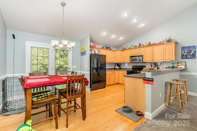 a kitchen with stainless steel appliances kitchen island granite countertop a dining table chairs and a refrigerator