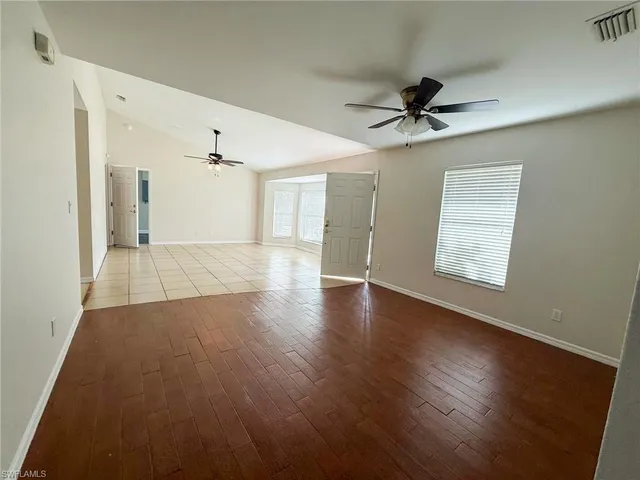 an empty room with wooden floor ceiling fan and windows