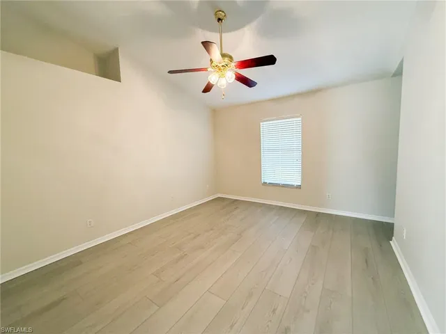 an empty room with wooden floor fan and windows