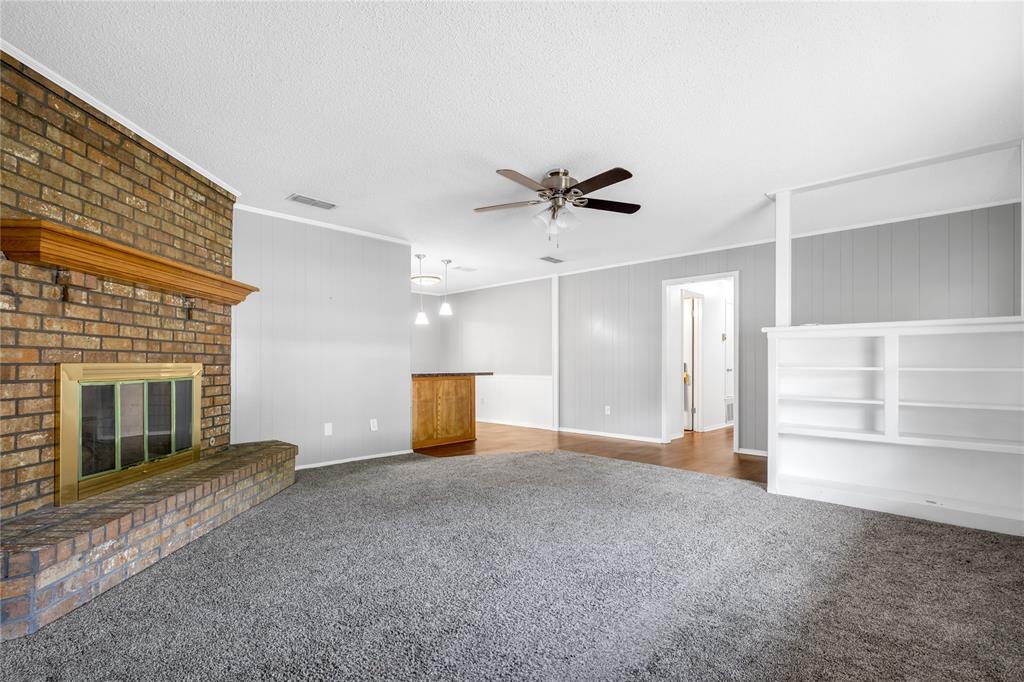 1609 Robin Street Mineola, TX 75773 - Photo 4 of 24 Spacious room featuring a brick fireplace with a wood mantle, built-in shelving, a ceiling fan, and carpet flooring