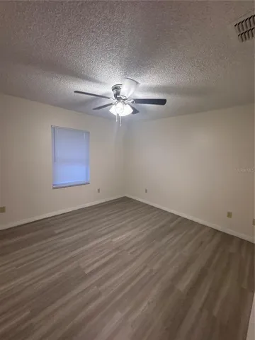 an empty room with wooden floor chandelier fan and windows