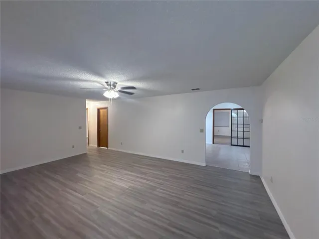 an empty room with wooden floor chandelier fan and windows