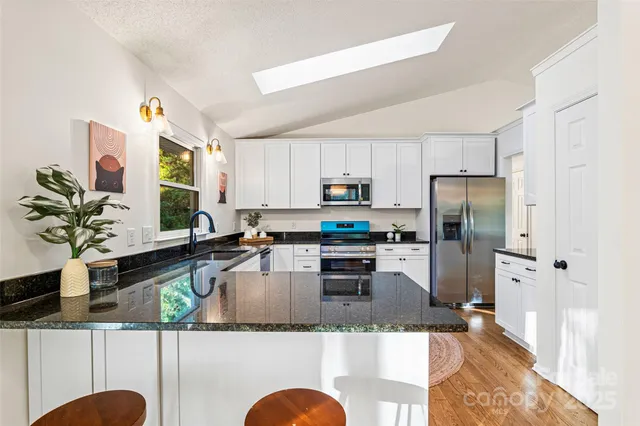 a kitchen with stainless steel appliances granite countertop a refrigerator a stove a sink dishwasher a dining table and chairs with wooden floor