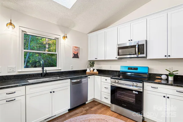 a kitchen with granite countertop white cabinets appliances a window and a sink