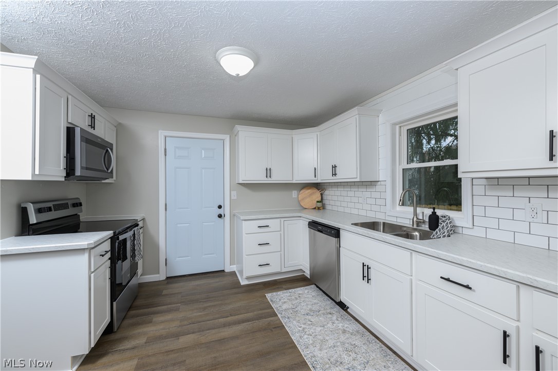 Kitchen with backsplash, white cabinets, stainless steel appliances, sink, and dark hardwood / wood-style flooring