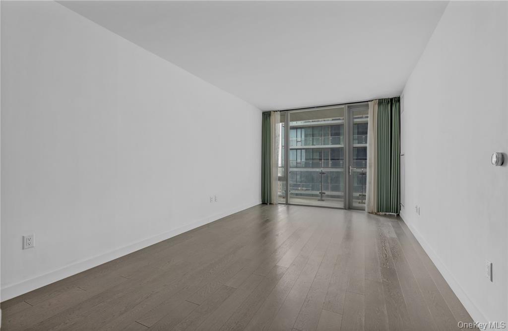 131-03 40 Road, Unit 16D Queens, NY 11354 - Photo 6 of 16 a view of an empty room with wooden floor and a window