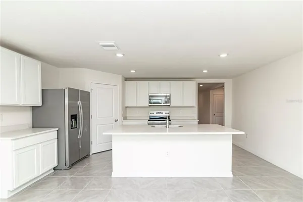 a dining hall with stainless steel appliances kitchen island a sink a stove a refrigerator with white cabinets