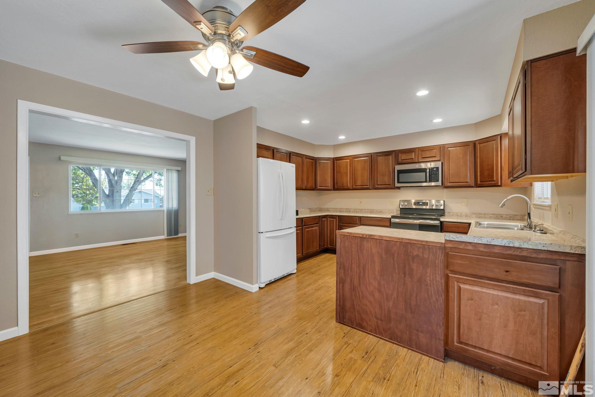 3240 Kings Row Reno, NV 89503 - Photo 6 of 31 a kitchen with stainless steel appliances granite countertop a refrigerator a sink dishwasher a stove top oven a dining table and chairs with wooden floor