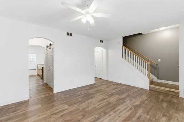 a view of an empty room with wooden floor and a ceiling fan