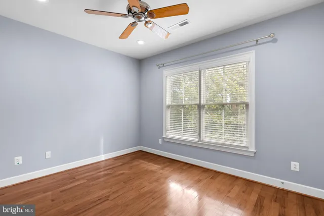 an empty room with wooden floor fan and windows