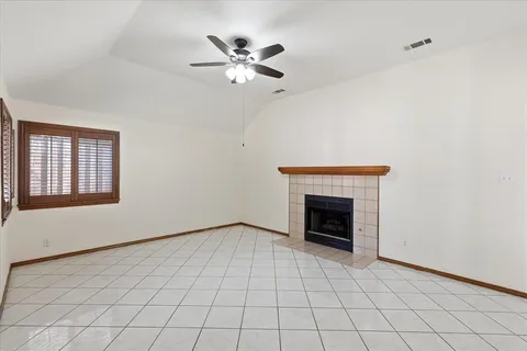 a view of an empty room with chandelier fan and fire place