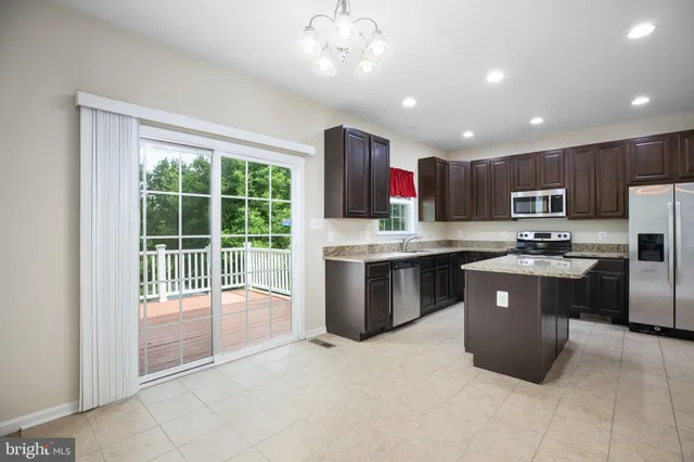 a kitchen with stainless steel appliances granite countertop a refrigerator a sink dishwasher a oven and a dining table with wooden cabinet