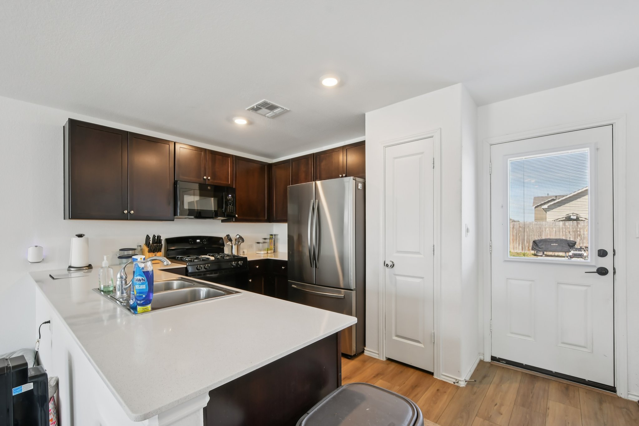 14116 Mussel Run Elgin, TX 78621 - Photo 13 of 40 Kitchen with black appliances, dark wood finish cabinetry, a peninsula, light wood-style flooring, and a breakfast bar