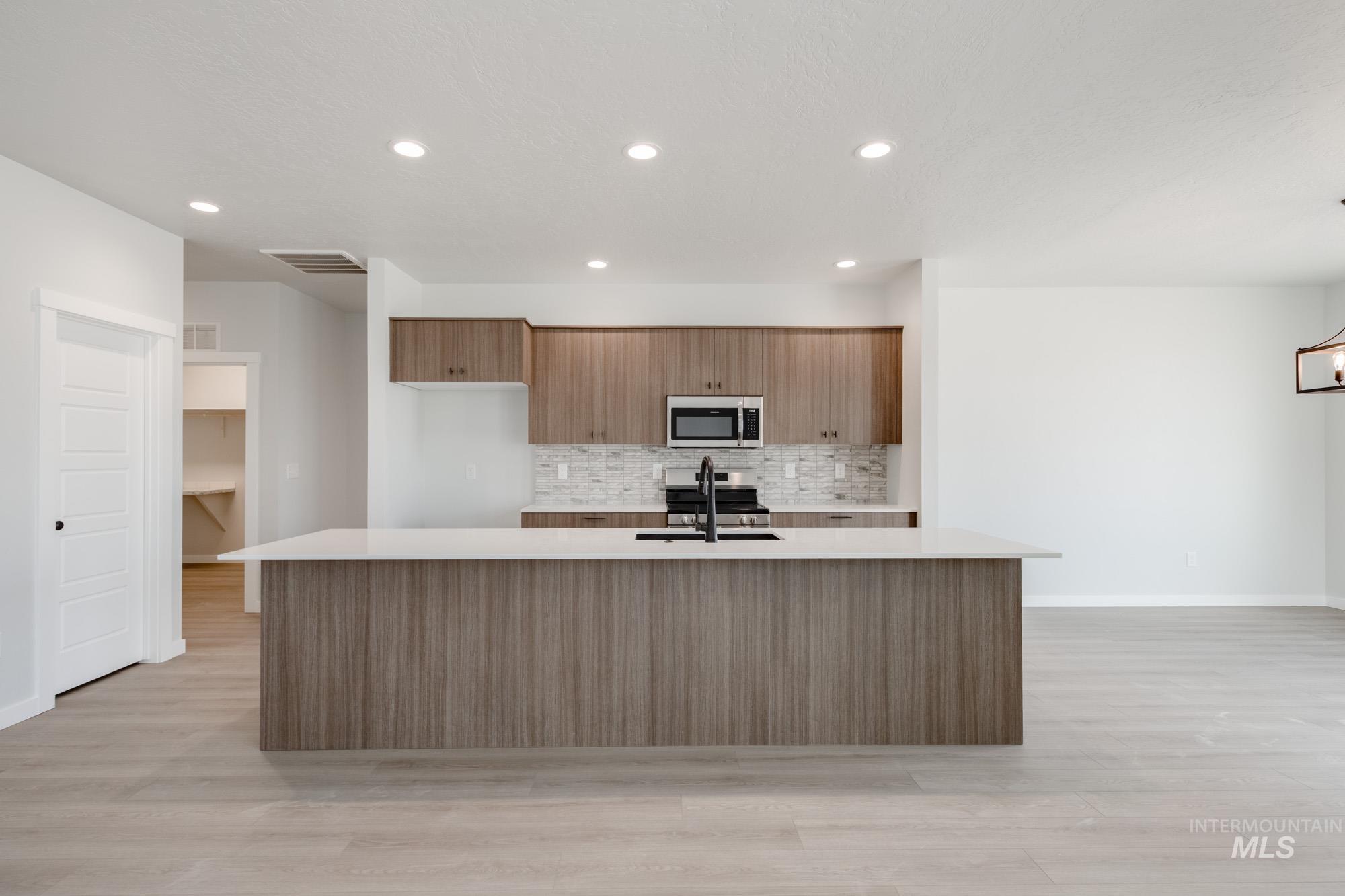 5131 Castleton Avenue Nampa, ID 83686 - Photo 4 of 25 Kitchen with tasteful backsplash, light countertops, light wood-type flooring, a spacious island, and appliances with stainless steel finishes