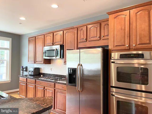 a kitchen with stainless steel appliances granite countertop a refrigerator a stove and a sink with large window