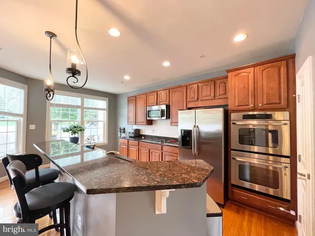 a kitchen with stainless steel appliances granite countertop a refrigerator a stove a sink a dining table and chairs with wooden floor