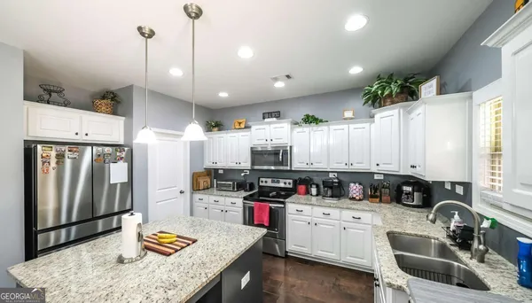 a large kitchen with granite countertop a stove a sink a refrigerator and white cabinets with wooden floor