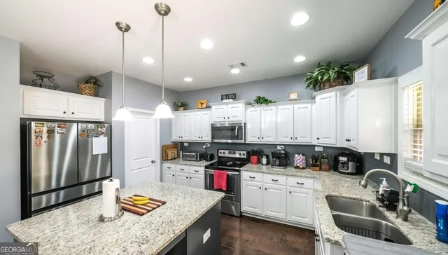 a large kitchen with granite countertop a stove a sink a refrigerator and white cabinets with wooden floor