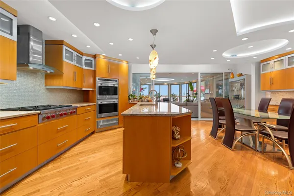 a kitchen with stainless steel appliances granite countertop a refrigerator a stove top oven a dining table and chairs with wooden floor