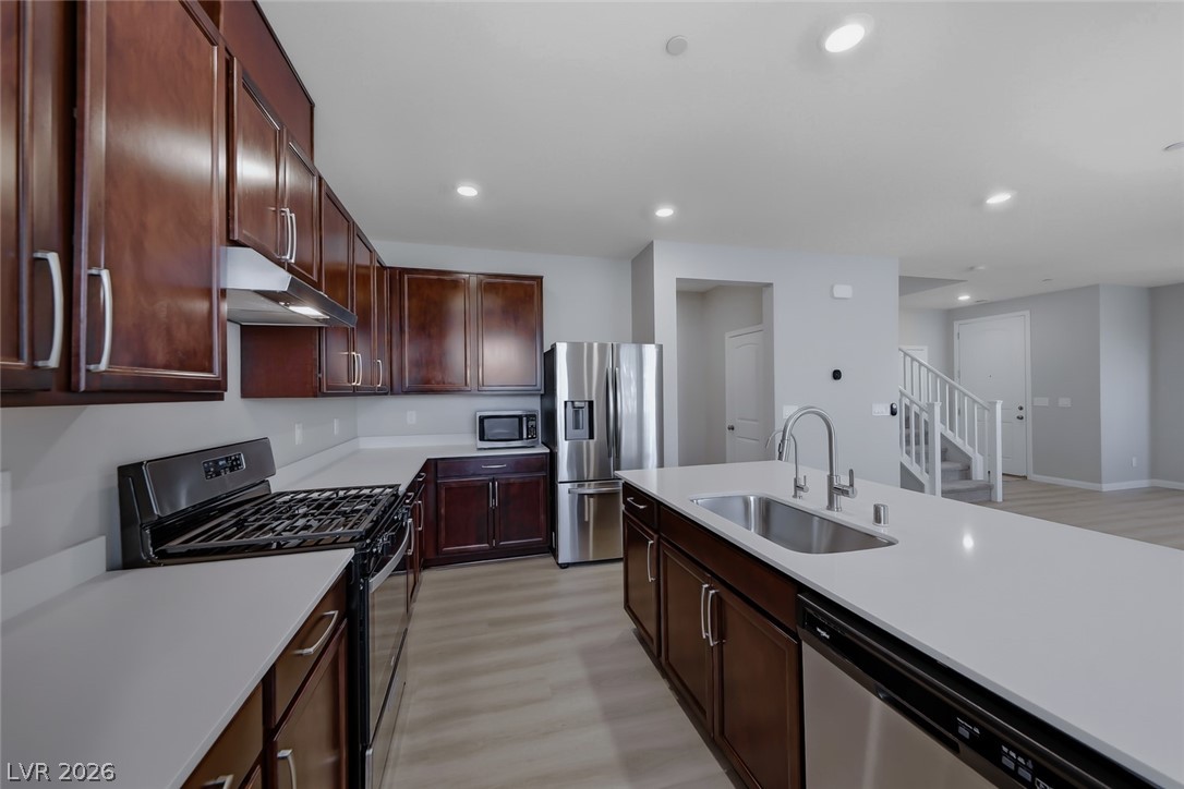 3564 Credere Lane Henderson, NV 89074 - Photo 4 of 40 Kitchen with stainless steel appliances, light wood-style flooring, recessed lighting, light stone counters, and dark wood finish cabinets