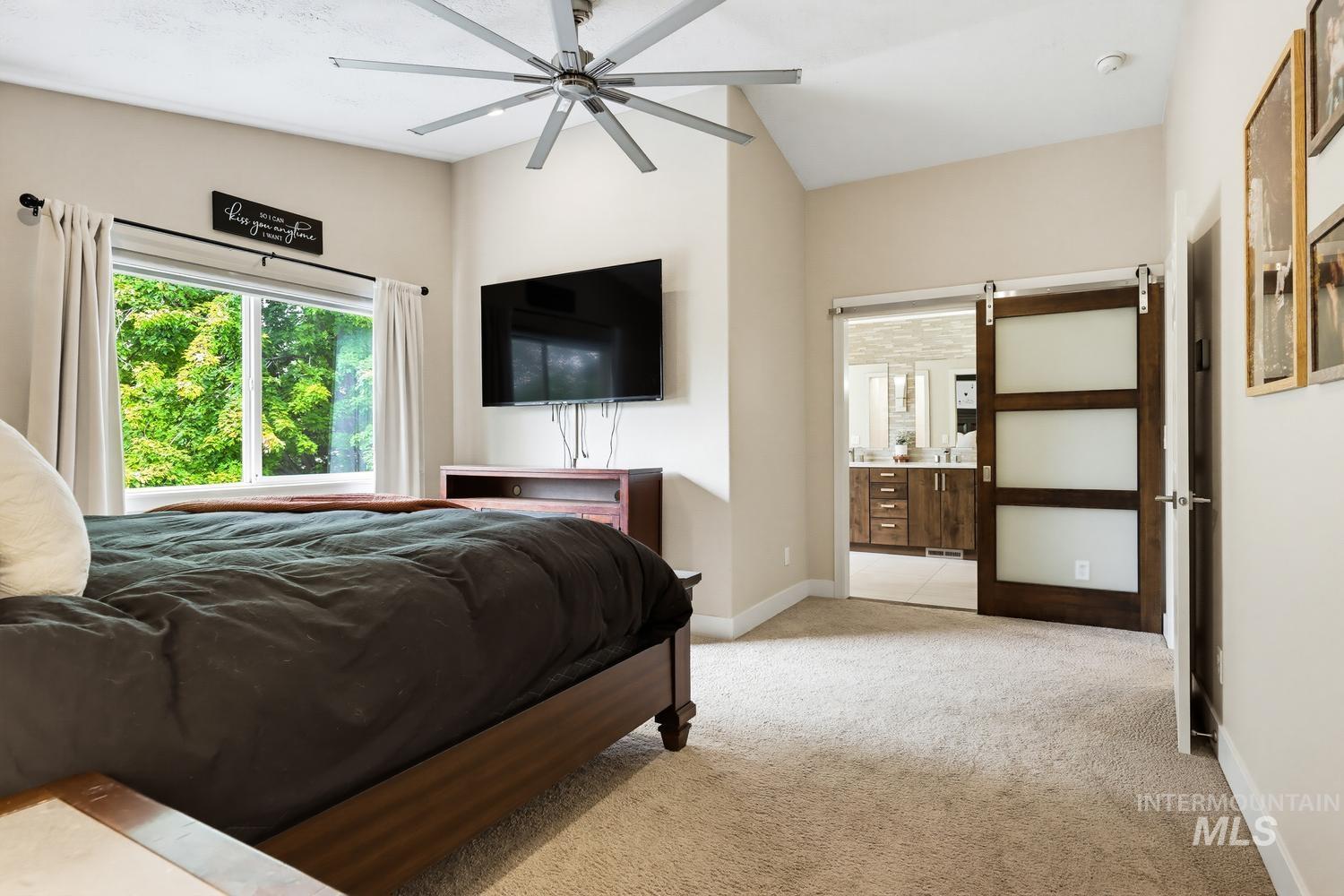 369 South Winthrop Way Boise, ID 83709 - Photo 27 of 50 Spacious room featuring vaulted ceilings, a large window, neutral carpet flooring, a barn-style door with frosted glass panels, and a modern ceiling fan
