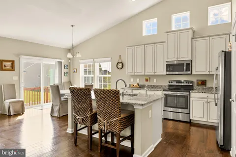 a kitchen with stainless steel appliances granite countertop a stove top oven a sink a dining table and chairs with wooden floor