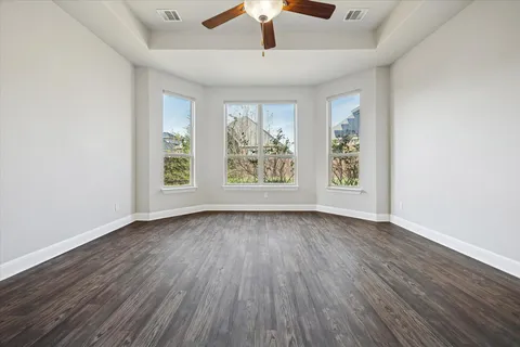 an empty room with wooden floor chandelier fan and windows