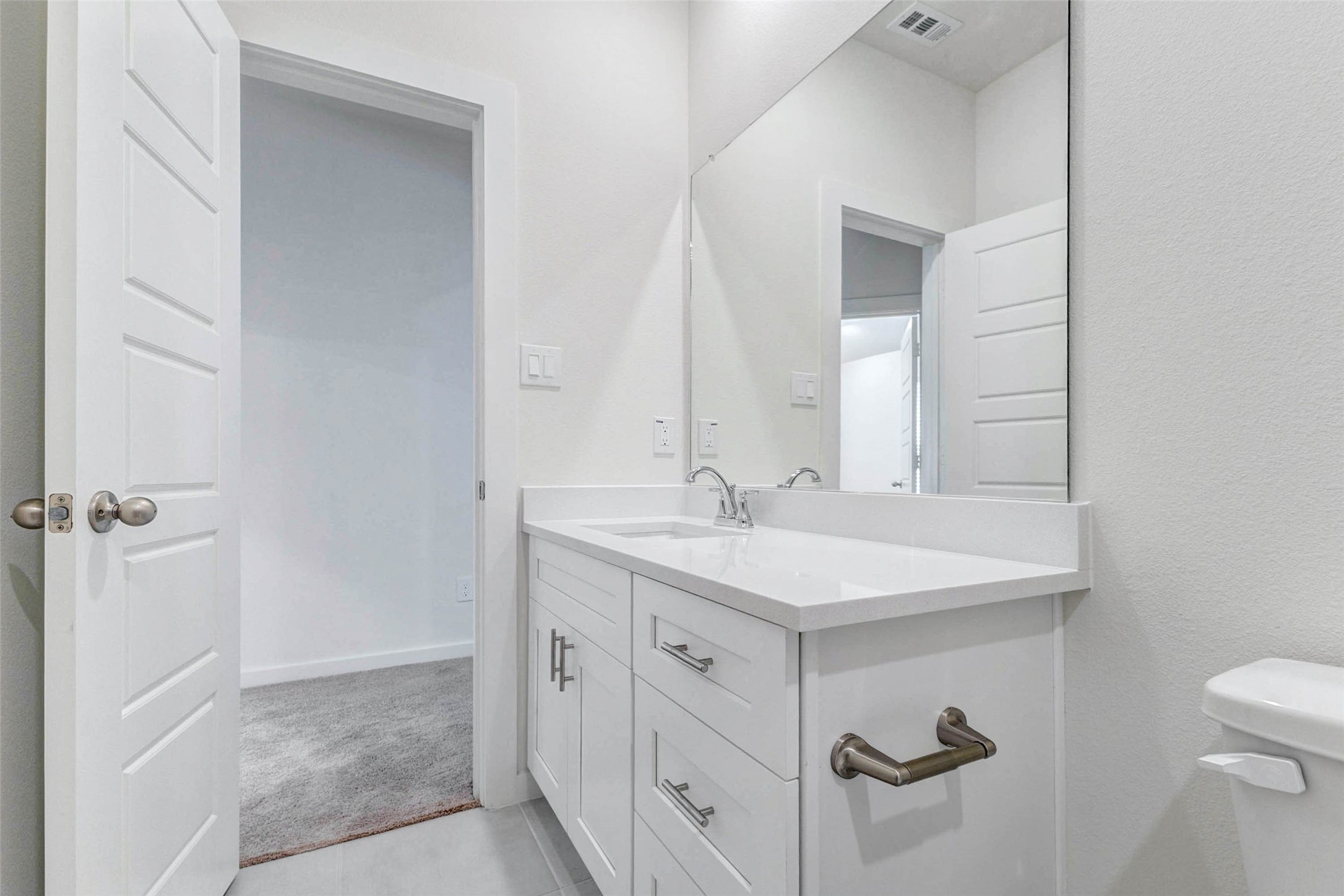 6475 Escondido Drive Rosharon, TX 77583 - Photo 27 of 32 Another view of the bathroom highlights the white vanity, modern hardware, chrome faucet, and spacious countertop. The large mirror helps the room feel open and bright, while the nearby doorway connects easily to the bedroom, making this bathroom both practical and convenient for everyday use.