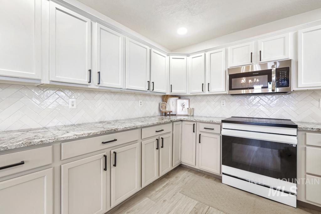 2243 4000 North Filer, ID 83328 - Photo 5 of 30 Kitchen with white range with electric stovetop, light stone counters, stainless steel microwave, white cabinets, and light wood-style floors