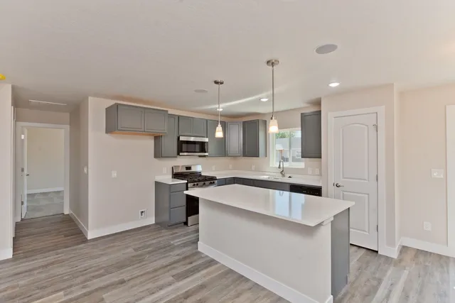 a large white kitchen with stainless steel appliances granite countertop a stove a sink dishwasher and a refrigerator with wooden floor