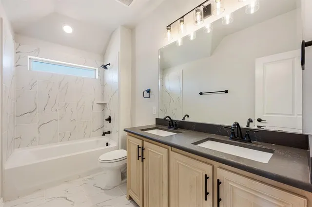 a bathroom with a granite countertop sink a toilet a mirror a bathtub and shower