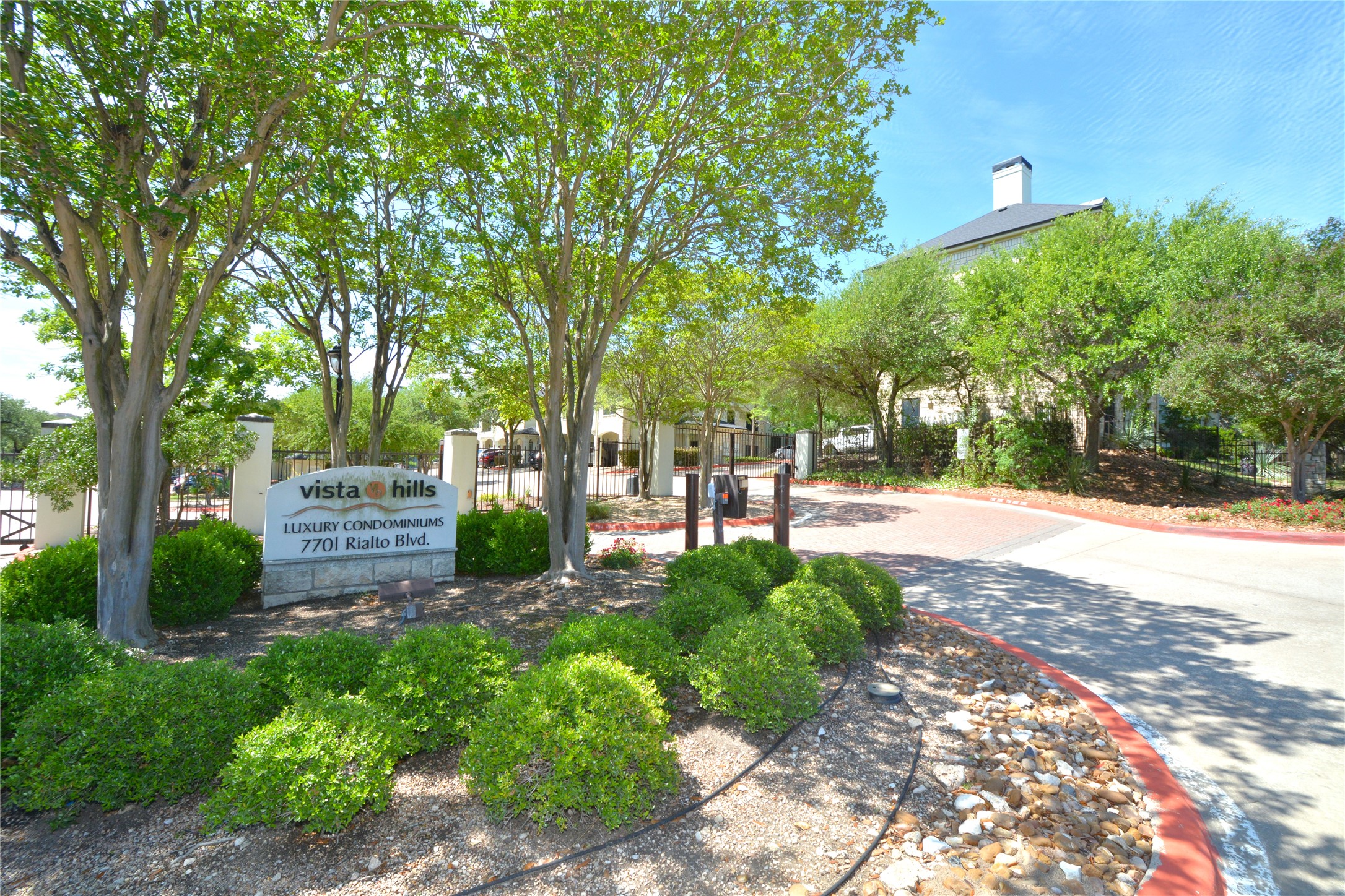 7701 Rialto Boulevard, Unit 124 Austin, TX 78735 - Photo 21 of 23 Stone-clad entry monument with "Vista Hills Luxury Condominiums" signage, surrounded by mature trees and manicured shrubbery
