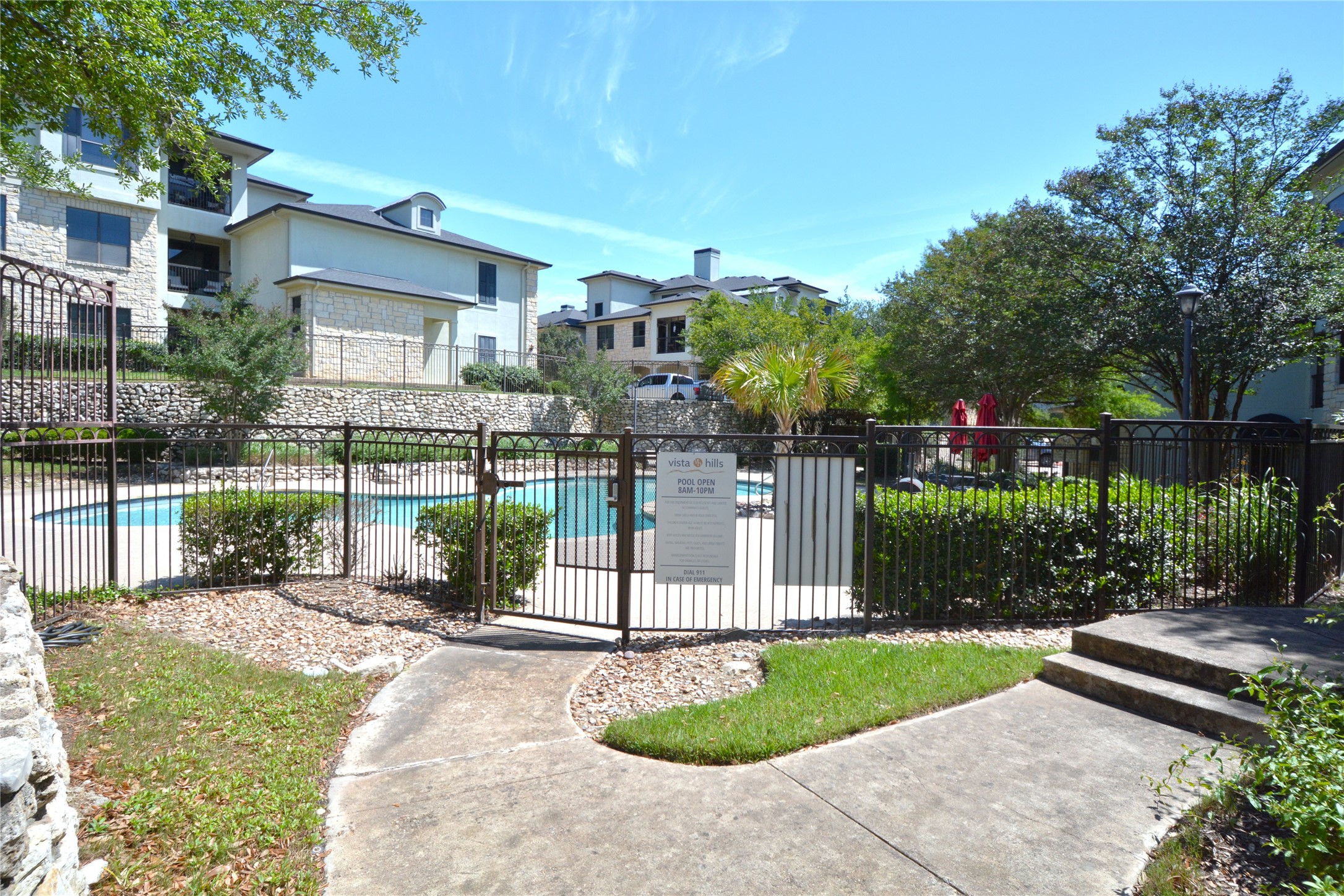 7701 Rialto Boulevard, Unit 124 Austin, TX 78735 - Photo 22 of 23 Community swimming pool surrounded by a black wrought iron fence and mature landscaping