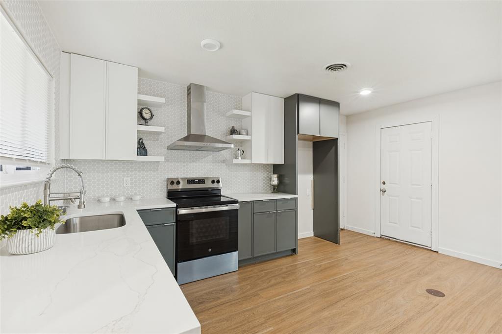 1215 Fordham Road Dallas, TX 75216 - Photo 11 of 25 Modern kitchen featuring light wood-finish flooring, white countertops, two-tone cabinetry, a stainless steel range hood, and a geometric tile backsplash