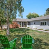 a backyard of a house with table and chairs potted plants and large tree