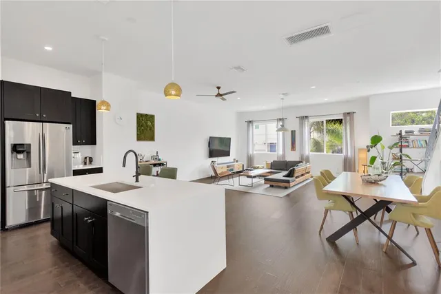 a open kitchen with stainless steel appliances kitchen island granite countertop a sink dishwasher a stove and a refrigerator with wooden floor