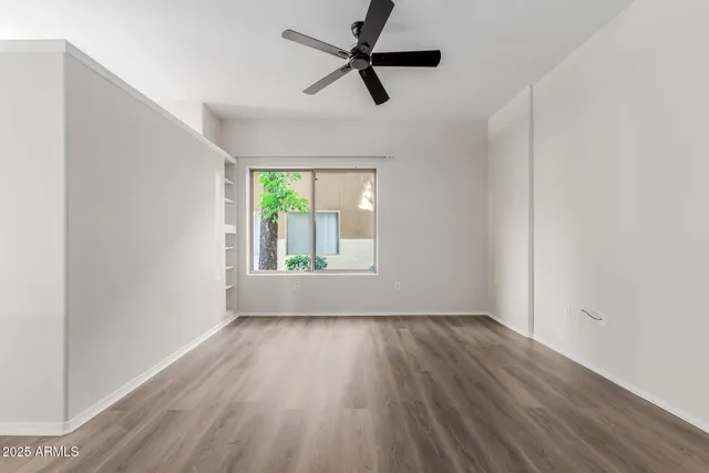 an empty room with wooden floor fan and windows