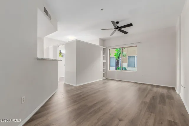 an empty room with wooden floor a ceiling fan and windows