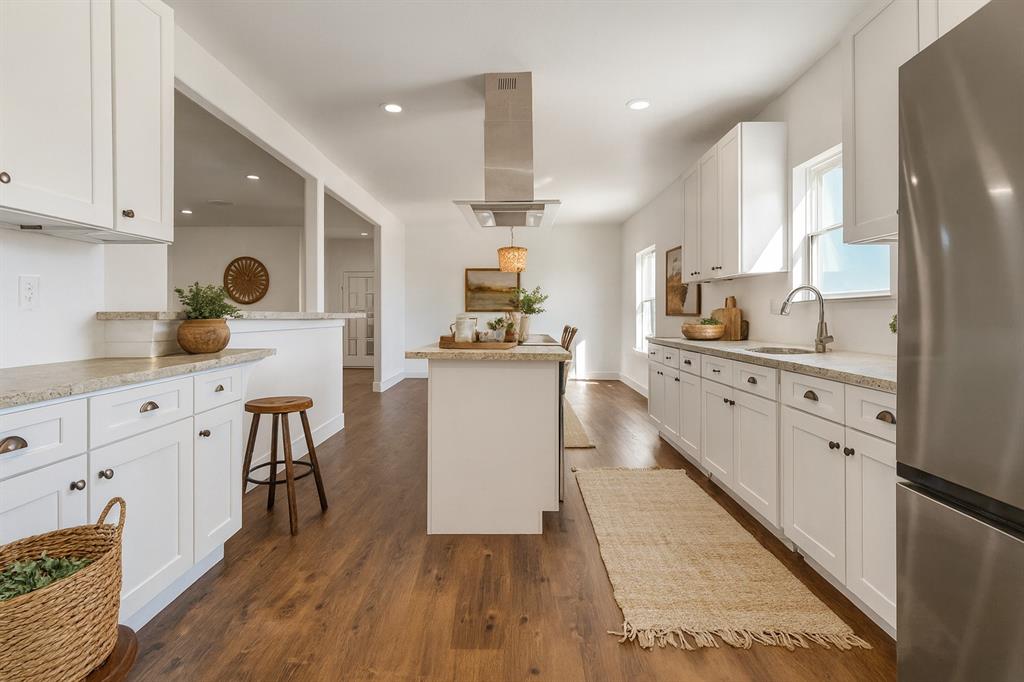 1128 Newton Road Ferris, TX 75125 - Photo 4 of 19 Kitchen with freestanding refrigerator, white cabinetry, island range hood, light stone countertops, and dark wood-style floors