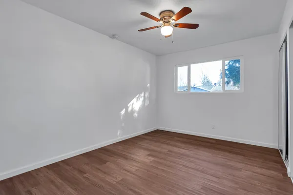 an empty room with wooden floor fan and windows
