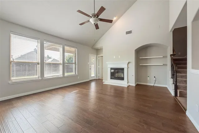 an empty room with wooden floor a ceiling fan and windows
