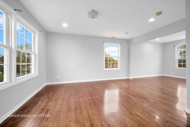 an empty room with wooden floor chandelier and windows