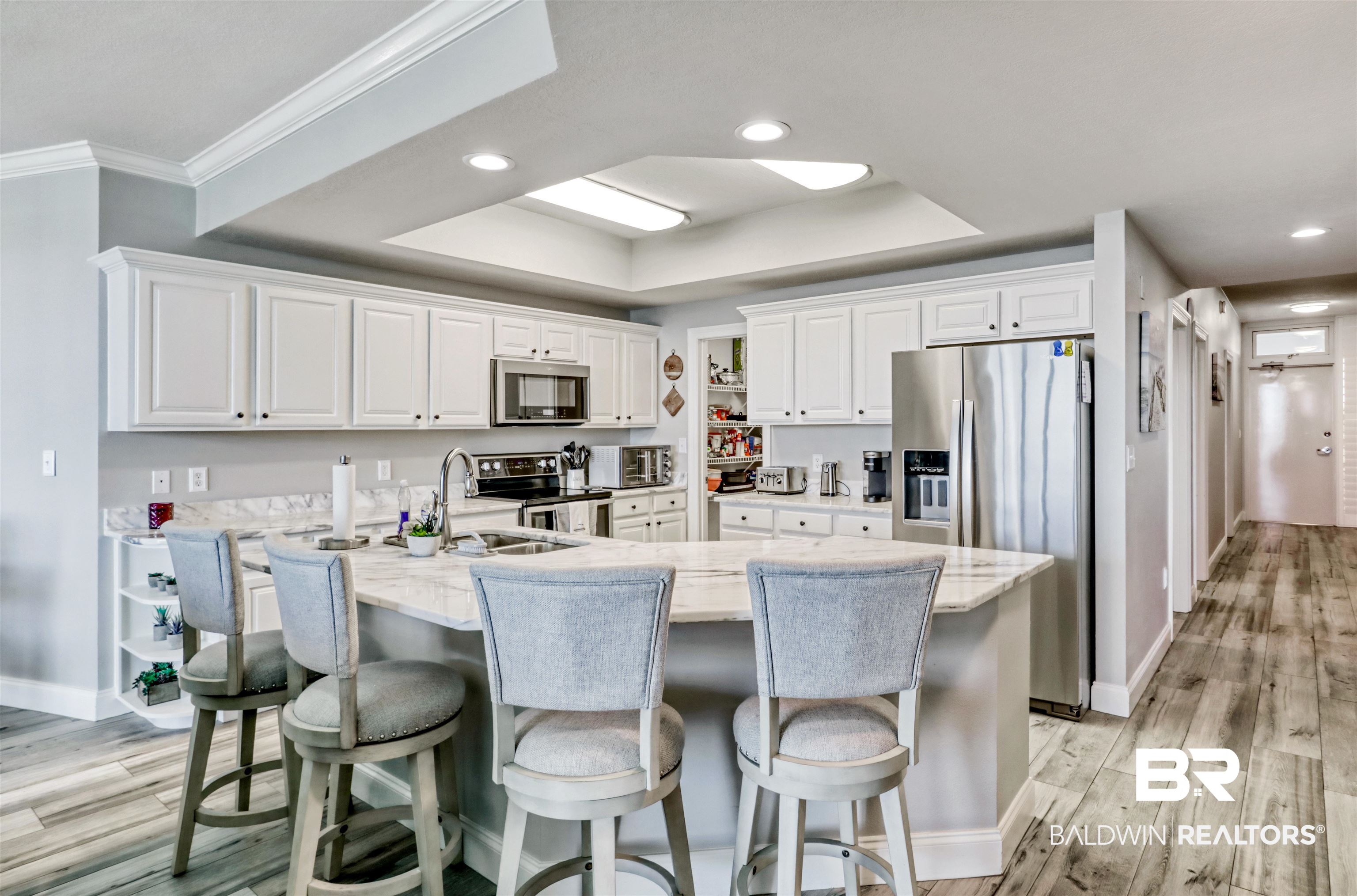 Kitchen with stainless steel appliances, white cabinetry, recessed lighting, a tray ceiling, and light wood-type flooring