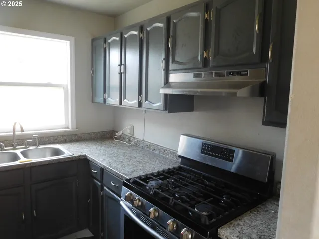 a kitchen with granite countertop a sink cabinets stainless steel appliances and a window