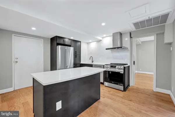 a view of an empty room with wooden floor and kitchen