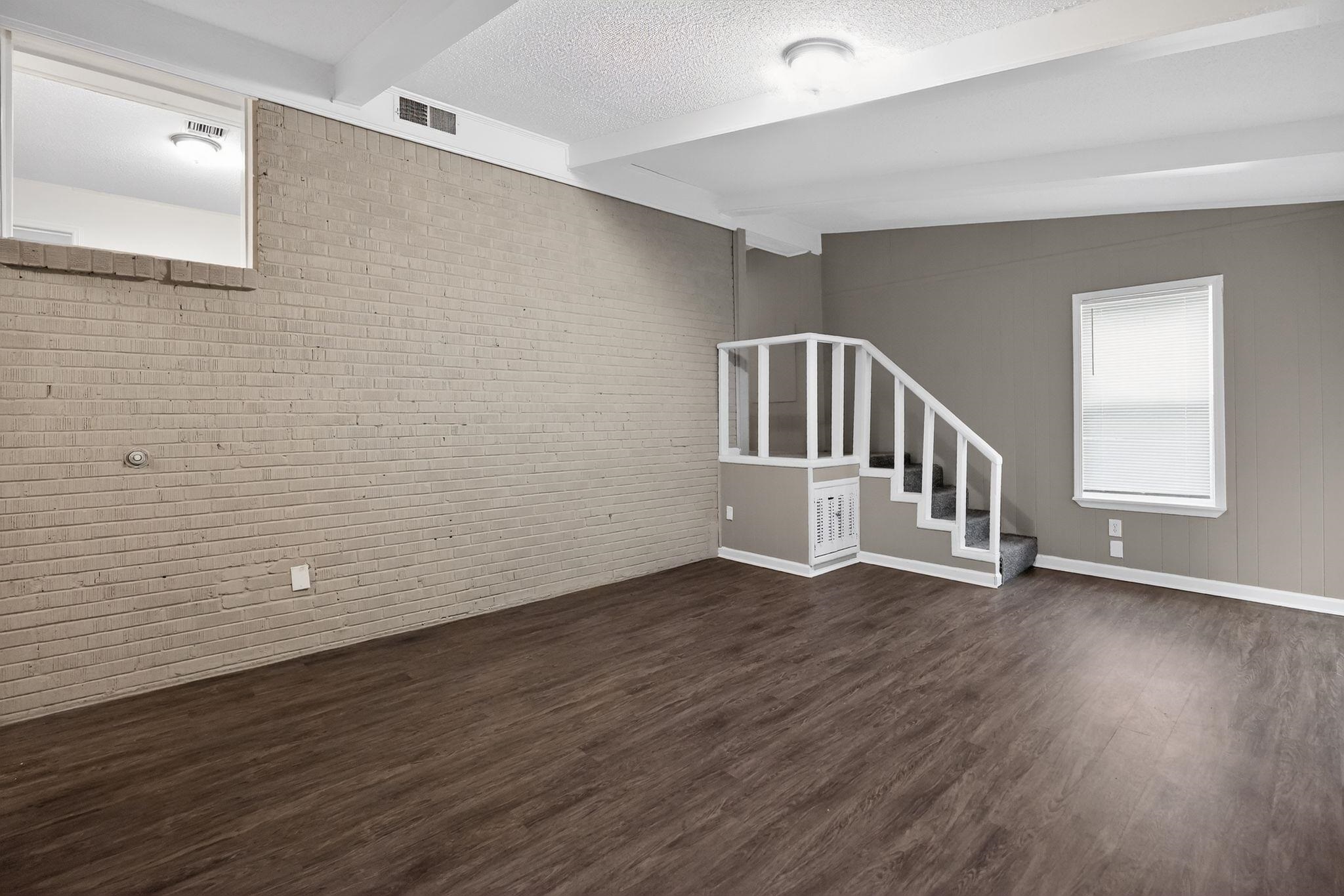 3603 England Street Memphis, TN 38127 - Photo 16 of 36 Unfurnished living room with brick wall, beamed ceiling, and dark wood-style flooring